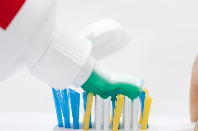 Studio closeup over white of a person applying toothpaste to the head of a toothbrush