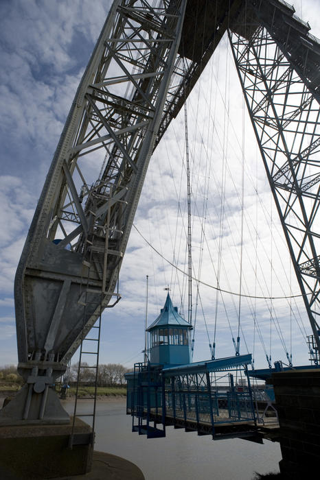 The gondola suspended below the metal span of the historical Newport Transporter Bridge ferrying cars and people acros the River Usk