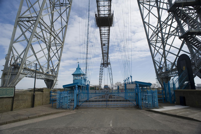 View of the entrance and along the tall steel span of the historic Transporter Bridge, Newport, Wales which relies on a motorised suspended gondola to ferry cars and people across the River Usk