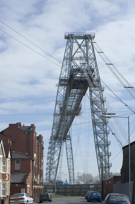 A view along an urban street of the very tall lattice steel span of the historic Transporter Bridge crossing the River Usk in Newport, Wales