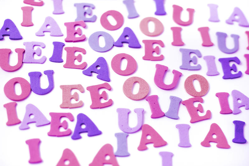 Colourful random collection of uppercase vowels in purple and pink on a white background for teaching young children the English language and to read, write and spell