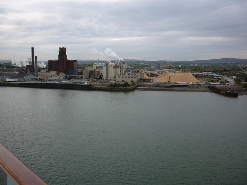 View across water to waterfront industrial buildings with chimneys releasing smoke into the air causing pollution, built near a waterway for ease of transport of manufactured goods