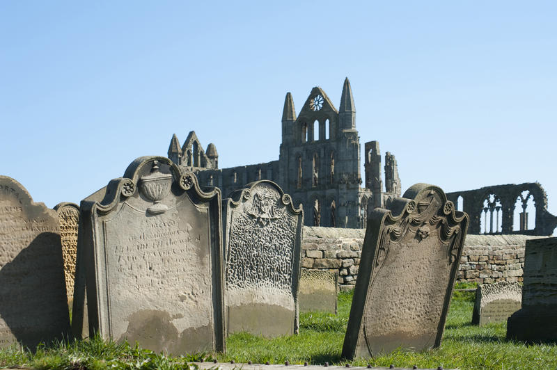 Ornate historical gravestones in front of the ruins of Whitby abbey on a beautiful sunny day with blue sky