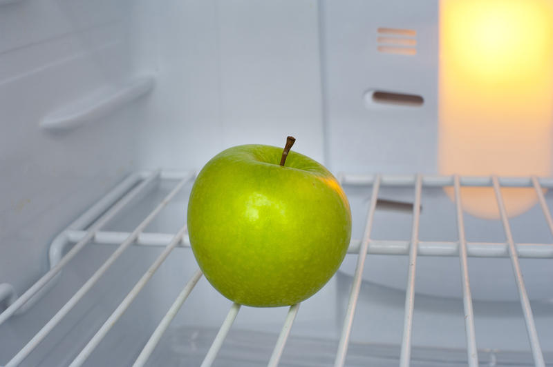 Single healthy green apple standing on a wire shelf in an empty fridge