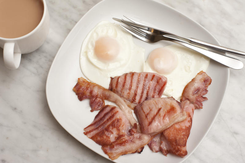 Fried eggs and with rashers of lean grilled bacon served on a plate with a mug of coffee, overhead view