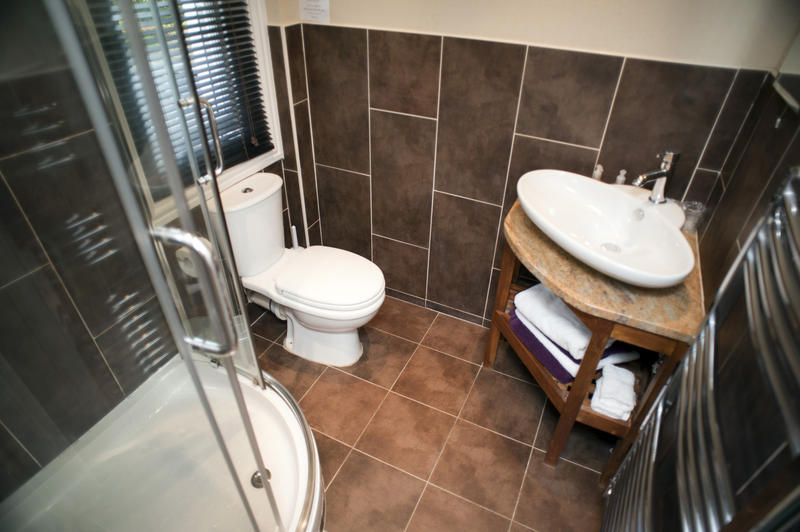 High angle interior view of a bathroom tiled in brown with corner hand basin, toilet and shower