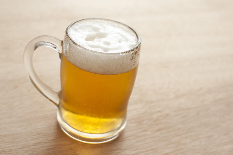 Glass tankard full of cold frothy beer standing on a wooden counter, high angle view with copyspace alongside