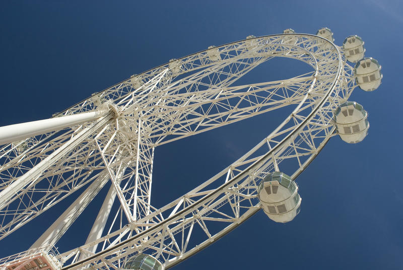 Large ferris wheel with passenger gondolas suspended from the metal rim on a fairground viewed from below against a clear blue sky