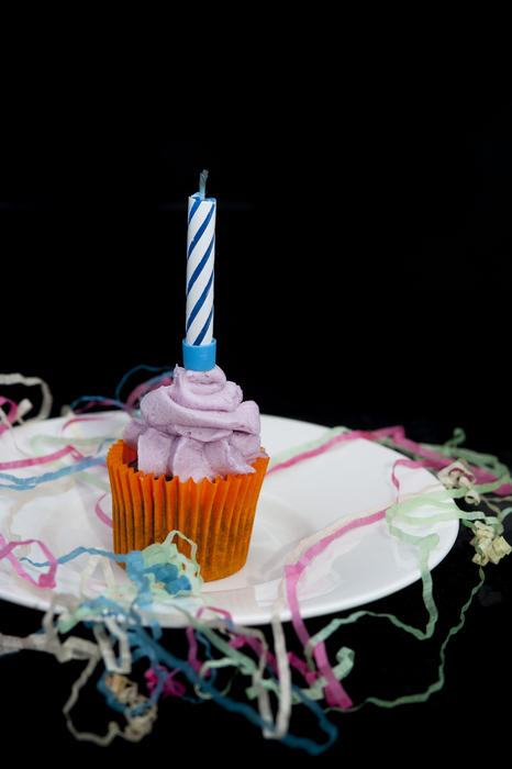 a samll cup cake and extinguisned candle with party streamers on black backgroung