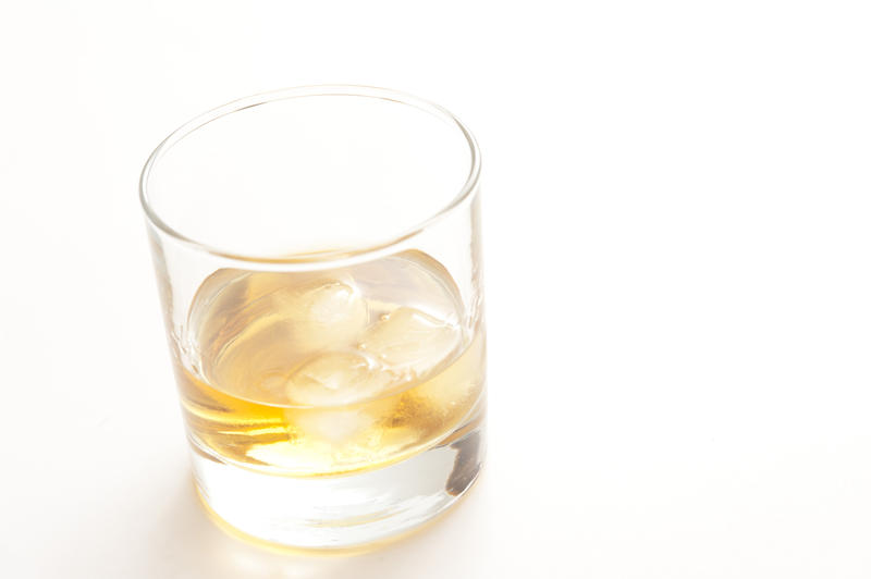 Bourbon whiskey served neat on ice in a plain glass tumbler for a relaxing alcoholic drink, on white