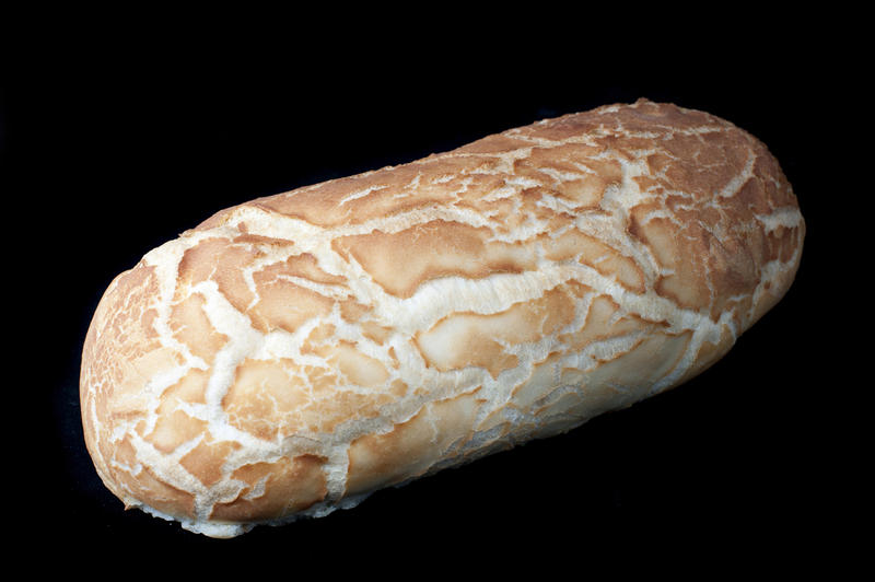 Uncut freshly baked white bread loaf with a crisp golden crust on a dark background