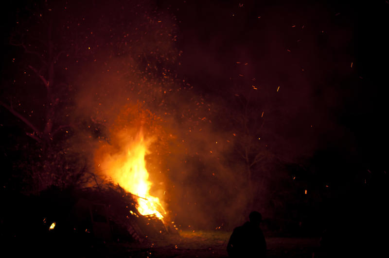 Burning bonfire in a field with bright orange flames shooting high into the night sky as people prepare to celebrate Bonfire Night or Guy Fawkes