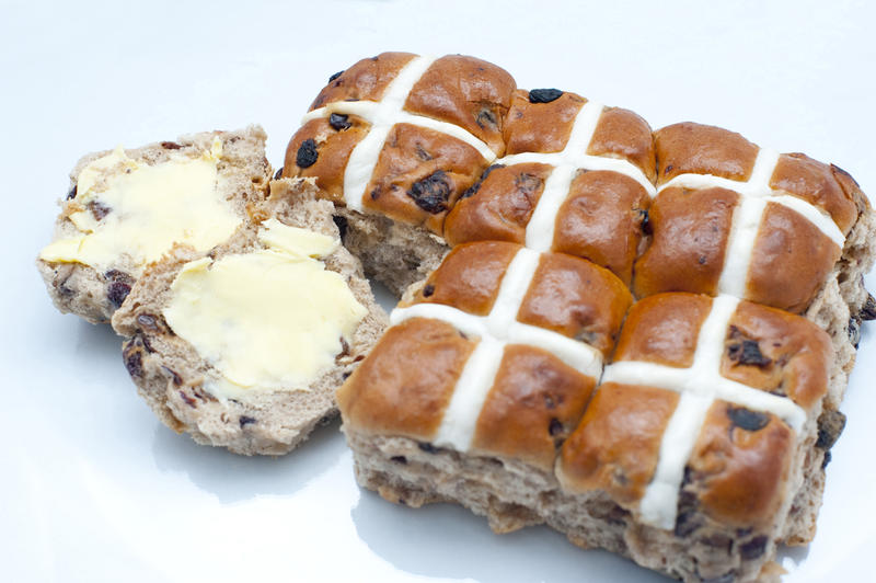 Overhead view showing the symbolic Easter crosses on a freshly baked batch of Hot Cross Buns with a buttered one separated off