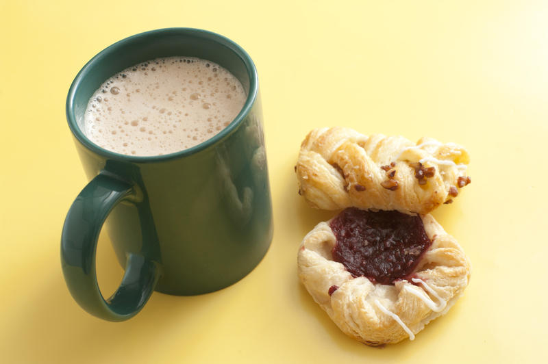 High angle view of a frothy mug of cappuccino coffee with two fresh pastries or biscuits on a yellow background