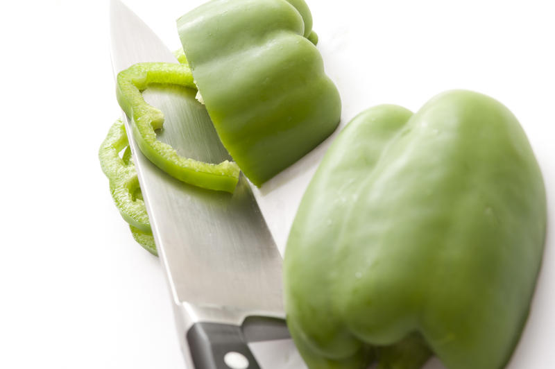 Slices of fresh green capsicum or bell pepper resting on the blade of a sharp kitchen knife during preparation for use in salads