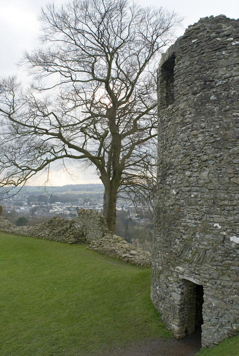 View past the ruined stone wall and tower at Kendal Castle, Cumbria, England to a bare branched tree and the countryside and town beyond