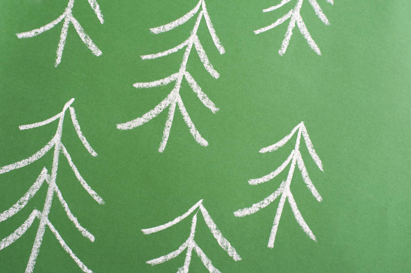 Chalk forest doodle sketch on a green chalkboard with simple stylised pine trees in a tilted pattern for a Christmas or nature themed background
