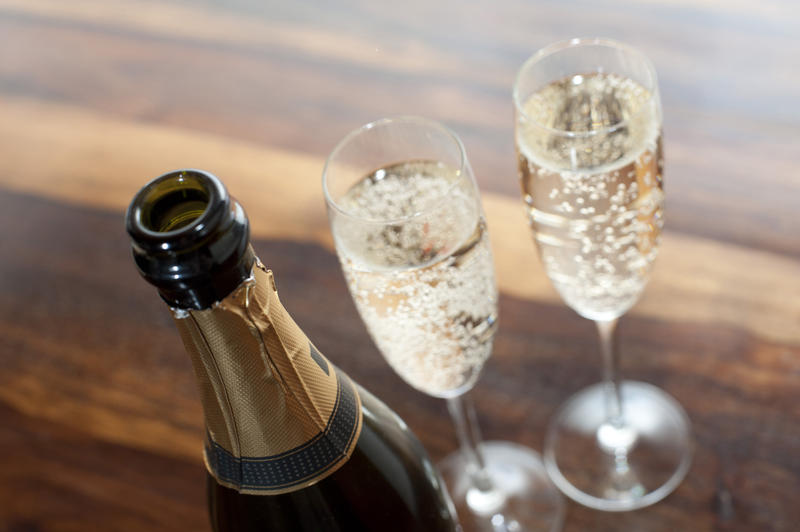 Two flutes of sparkling romantic champagne standing alongside a champagne bottle on a wooden table for a special occasion and celebration, high angle close up view