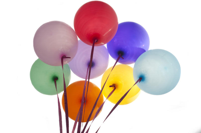 Bunch of colorful party balloons in the colors of the rainbow tied with ribbons floating in the air, isolated on white