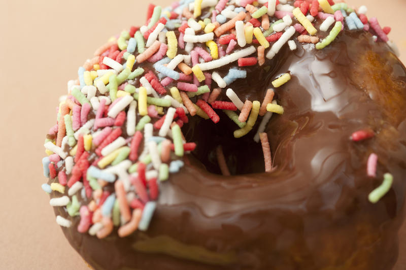 Chocolate glazed donut or doughnut dipped in multicolored sprinkles for a tasty tea or coffee break snack, closeup view