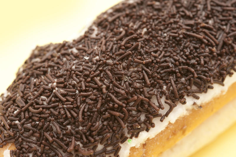 Chocolate sprinkles on an iced sticky cream bun, close up view of the texture