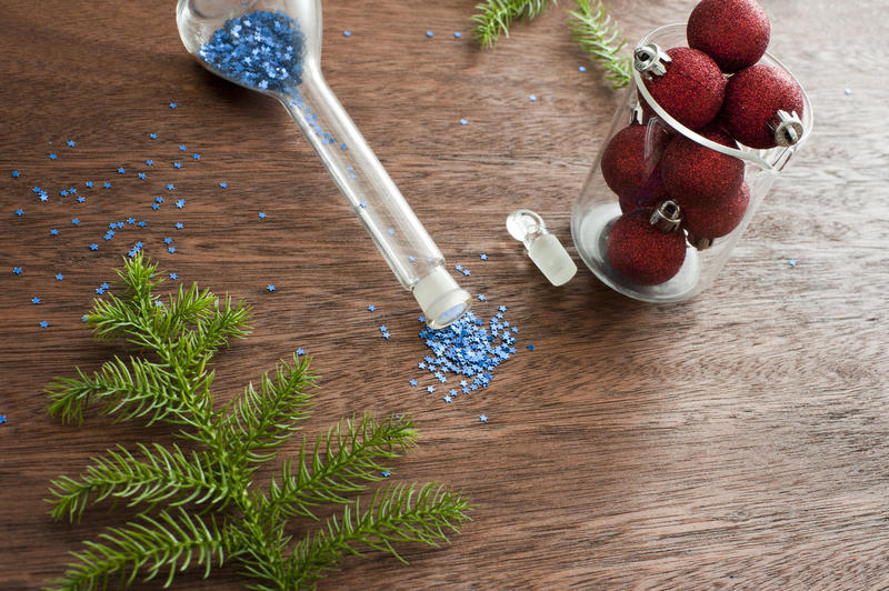 Christmas concepts with modern decoration components on a wooden table including blue glitter in a flask, red baubles in a glass jar and a fresh green pine frond