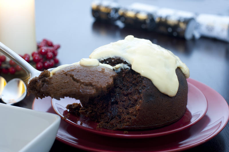 Serving a delicious steamed fruity Christmas pudding topped with brandy sauce at a festive Xmas dinner table