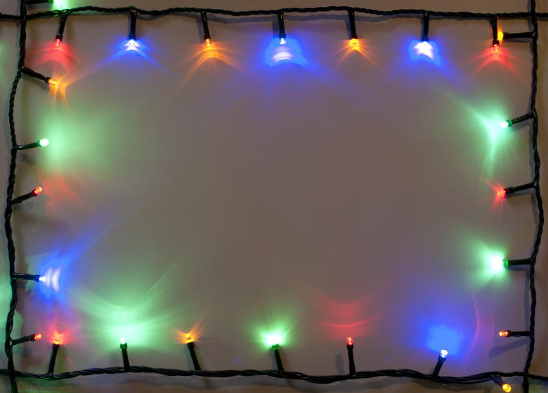 Colorful shining Christmas light border with red, blue and green lights on a string around central copyspace for your greeting
