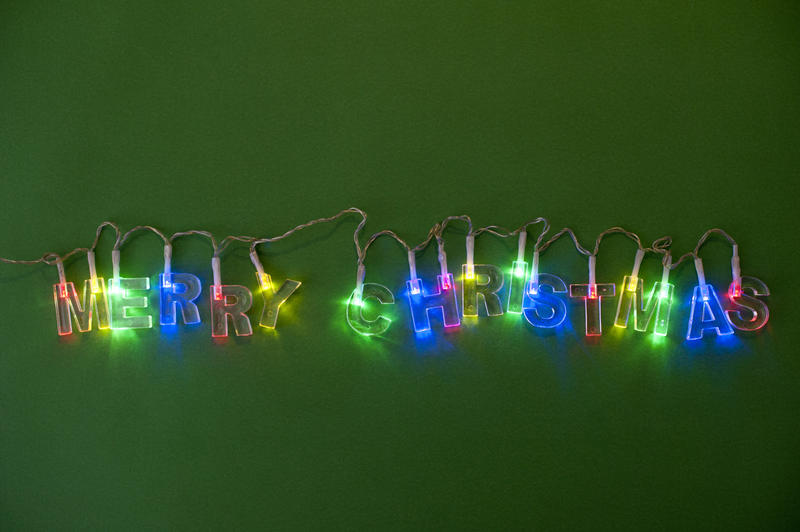 Colorful garland of Christmas lights in multiple colors sparkling on a dark green background, with copyspace above and below