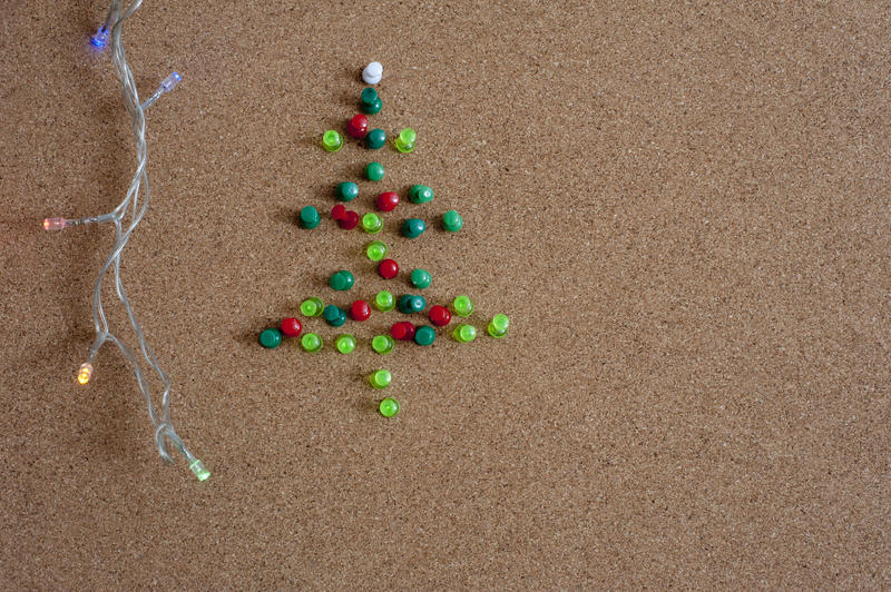 Festive Christmas office concept with a decorative Christmas tree formed of thumb tacks on a cork board with a string of dangling lights, copyspace to the right for your seasonal greeting