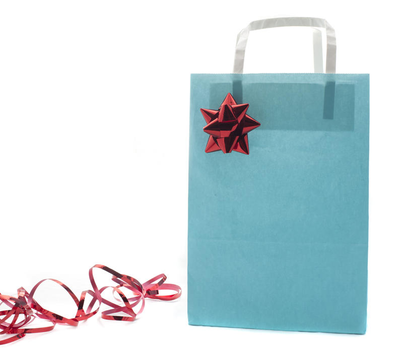 Close-up of a blue paper bag decorated with a shiny red ribbon, symbol of Christmas presents, on white background
