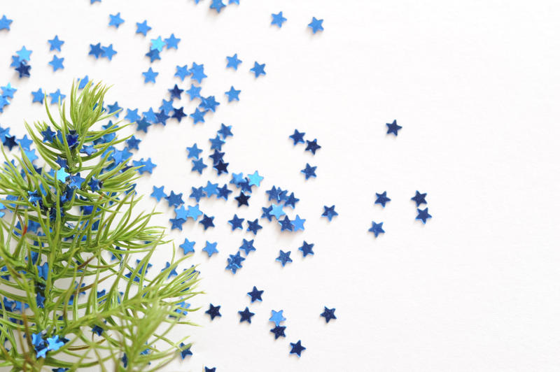 Christmas card background with a fir branch and colorful blue stars scattered across a white background with copyspace for your seasonal greeting