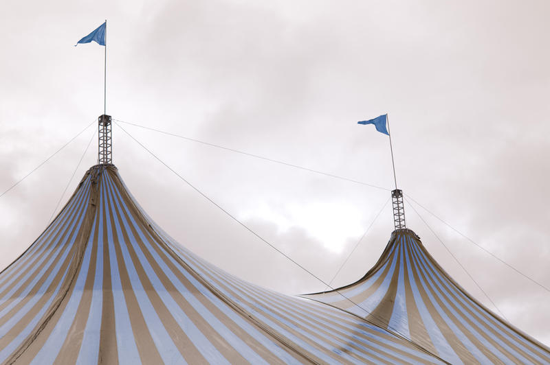 Colorful striped red and white Big Top tent at a circus flying two flags from the centre poles against a cloudy sky