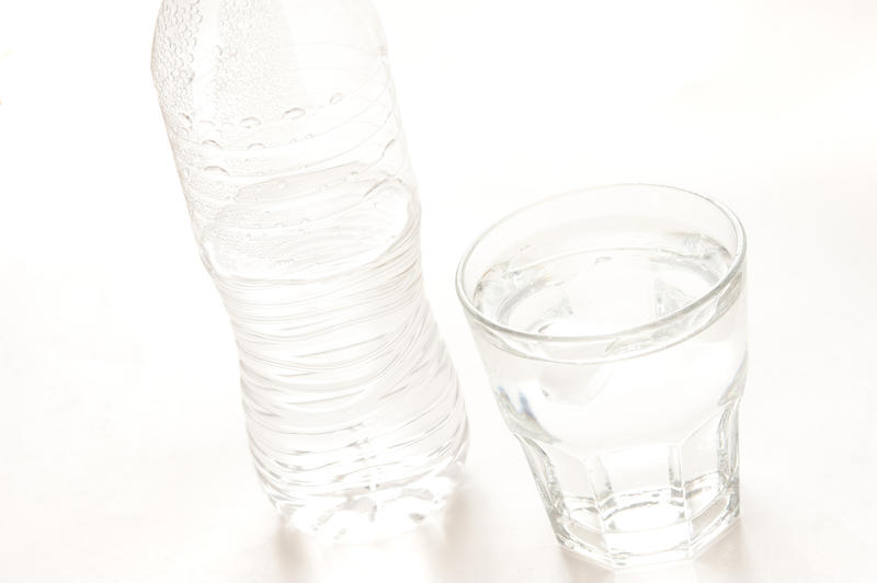 Glass of fresh clean water standing alongside a plastic water bottle on a white background