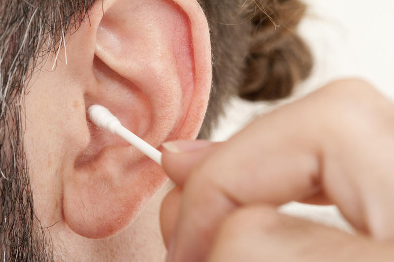 Person cleaning wax out of their ear using a clean cotton bud in a personal hygiene and health concept