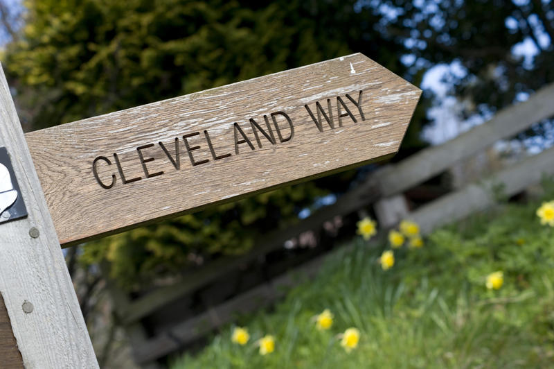Wooden Cleveland Way signpost pointing in the direction of the footpath running along the top of the scenic North Yorkshire coastal cliffs
