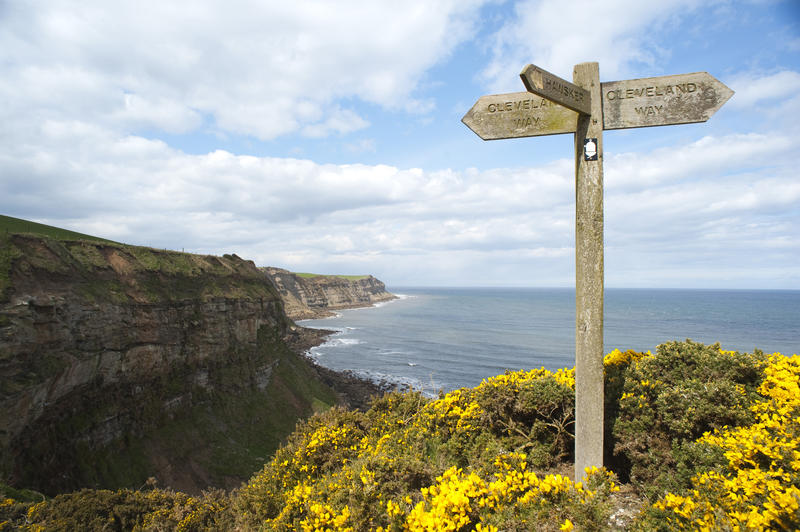 Old wooden signpost on the cliff top overlooking the ocean on Cleveland Way, a footpath running along the North Yorkshire coastline