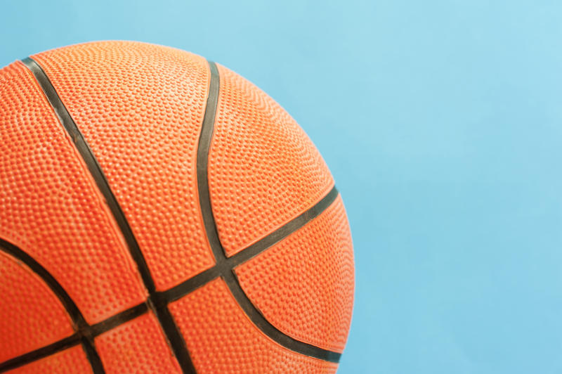 Close up Textured Orange Basketball Ball with Black Lines Isolated on a Sky Blue Background
