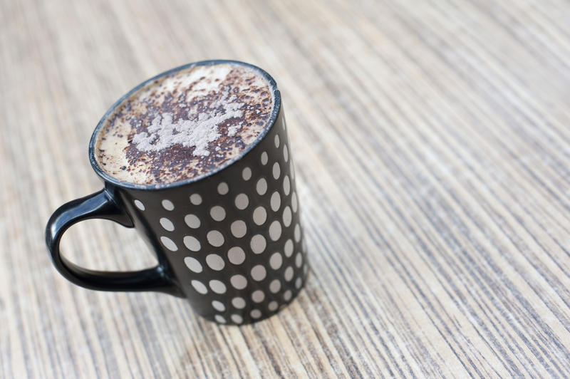 Close up Black Cup with White Polka Dots Design Filled with Full of Coffee on Top of Wooden Table.