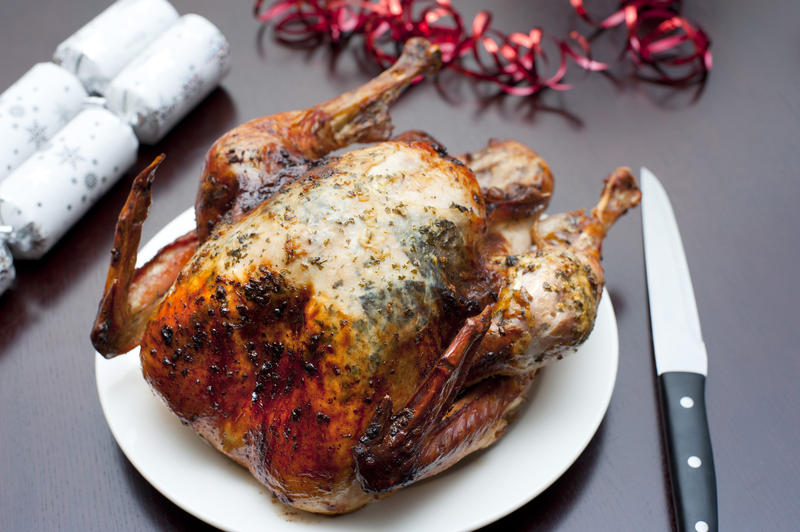 Whole roast Christmas turkey served ready on a plate for carving alongside festive crackers and table decorations