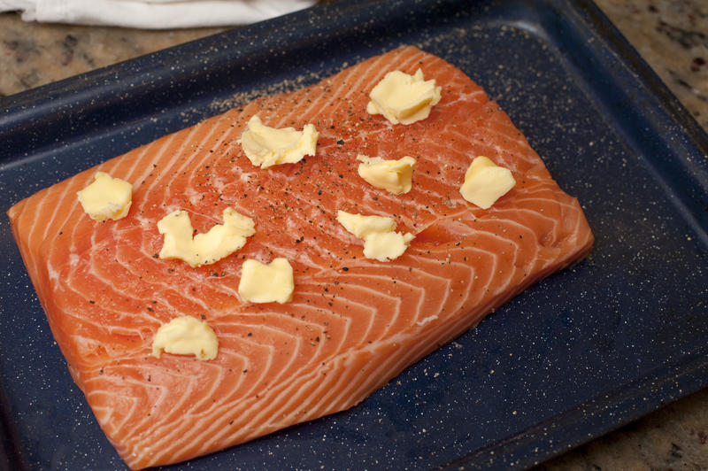 Cooking a fresh portion of salmon with a high angle view of the fish in a baking tray daubed with butter ready to be grilled or baked
