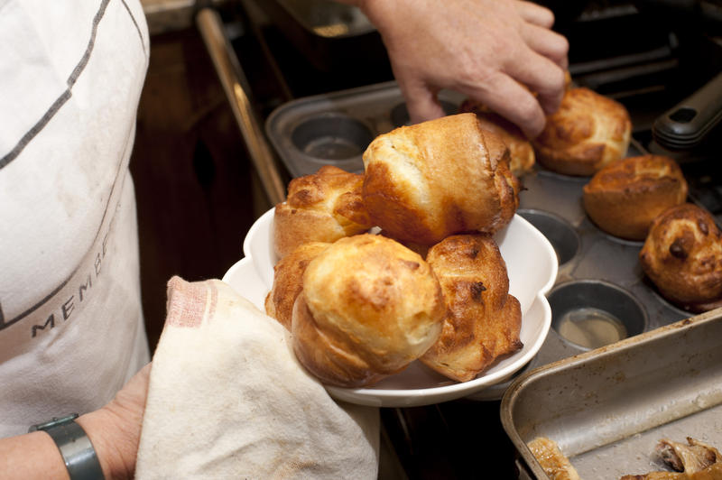 Cooking Yorkshire Puddings made from a light batter removing them from the baking tray to serve as an accompaniment to roast beef