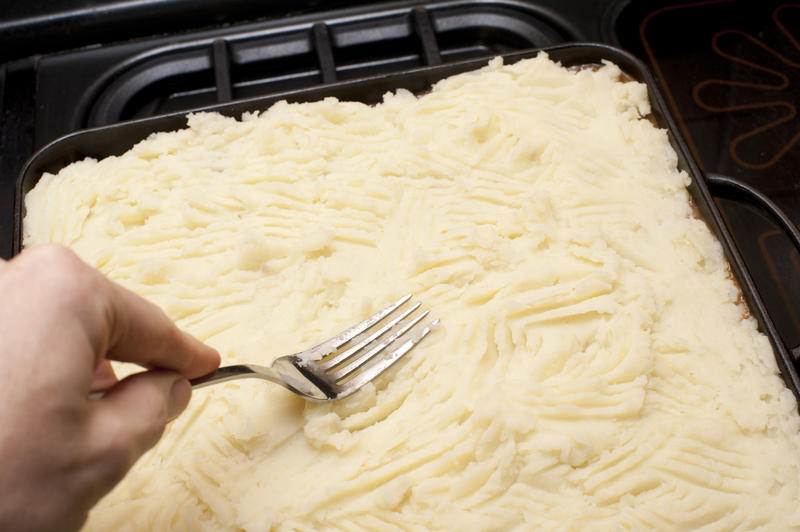 Preparing a cottage pie for dinner as a man uses a fork to press the mashed potato crust into position before placing it in the oven to grill or bake