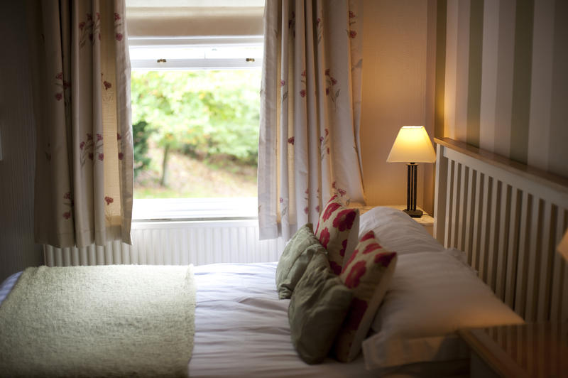 Country bedroom with a view over a comfortable double bed to a window overlooking a leafy green garden