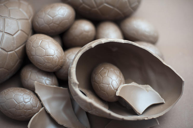 Cracked milk chocolate Easter egg accompanied by a collection of various sized eggs on a brown background