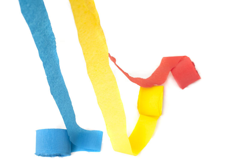Crepe streamers for a party celebration in colorful red, yellow and blue still partially rolled over a white background with copyspace
