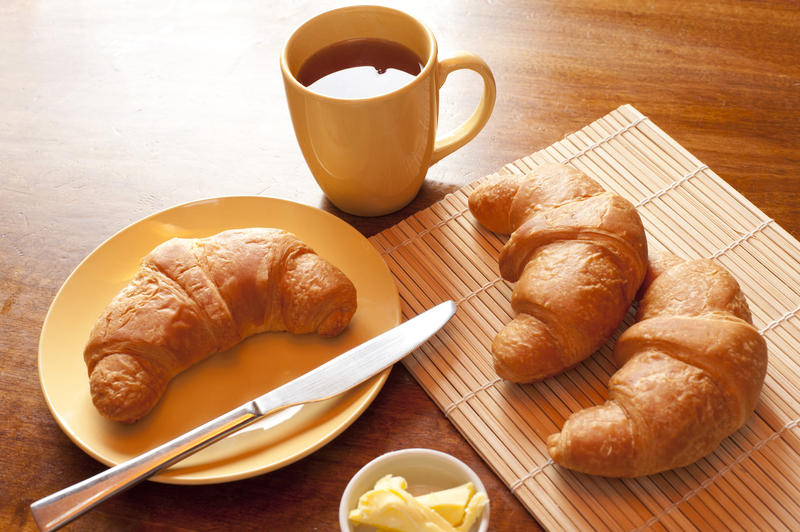 French delicious breakfast with croissants, butter and a cup of tea, on a wooden table