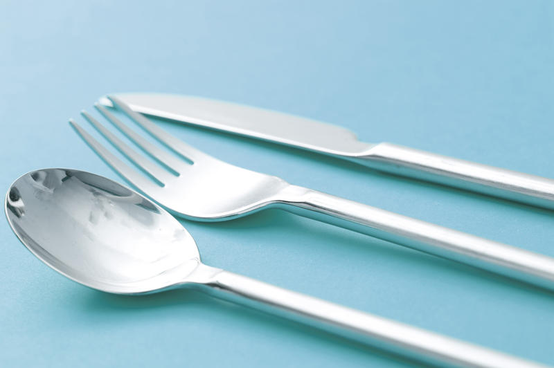 Close up Set of Glossy Silver Cutlery with Spoon, Fork and Knife Isolated on a Cyan Background