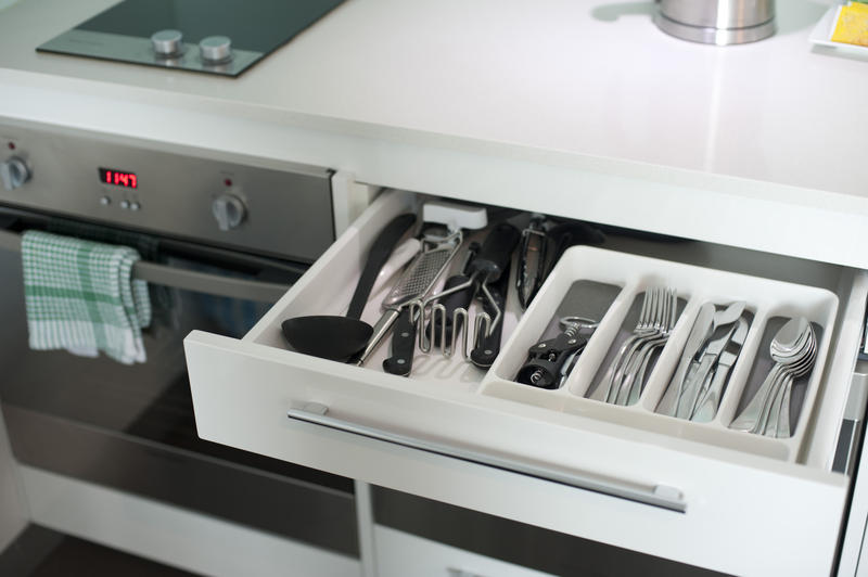Open cutlery drawer in a kitchen cabinet showing the internal compartments and neatly arranged utensils