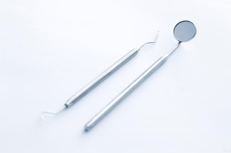 Dentists implements isolated on white with a stainless steel mirror and tooth pick arranged diagonally on white